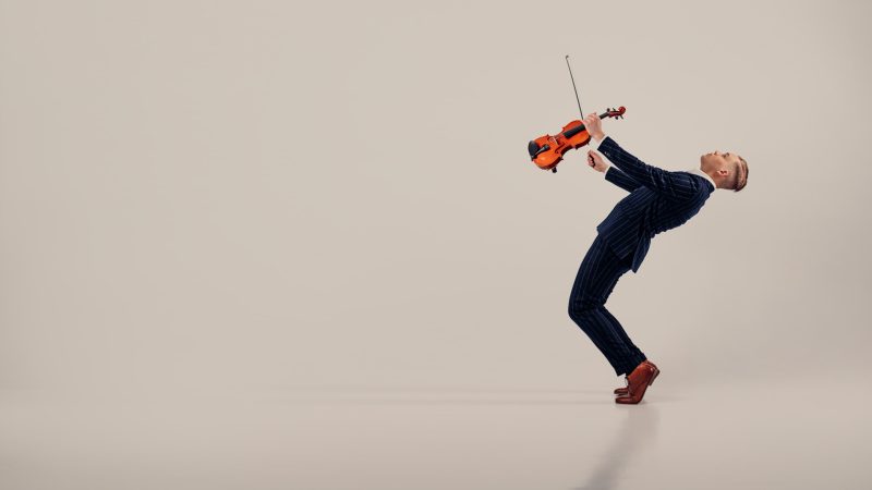 Mies taaksepäin vahvasti nojaten soittaa viulua kuvan oikeassa laidassa.