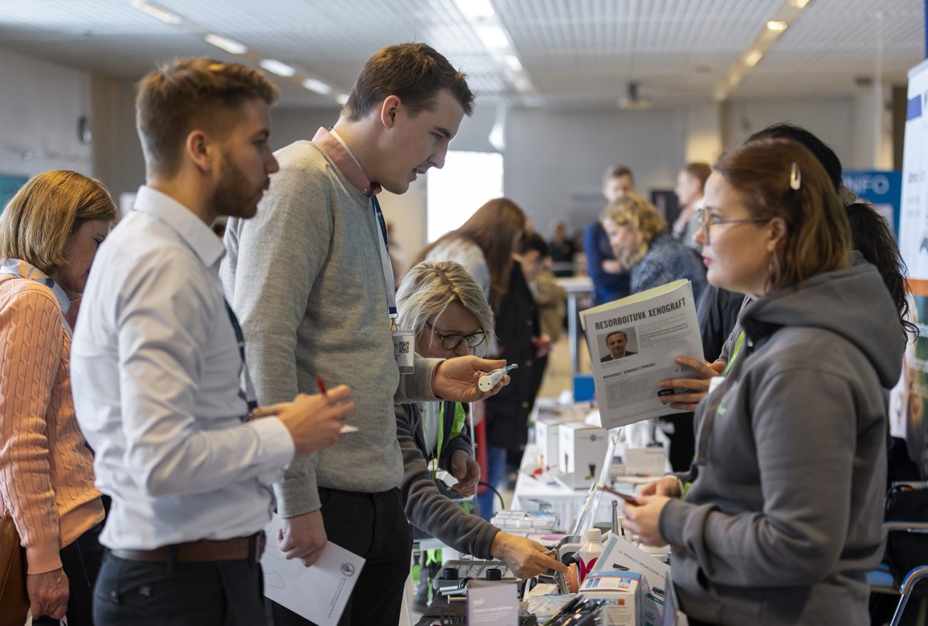 Ihmiset juttelevat Apollonia Symposiumin näyttelyalueella