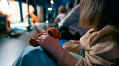 Nuorilapsi konsertia katsomassa. Lähikuvassa pieni pehmonalle, jota lapsi puristaa lujaa.