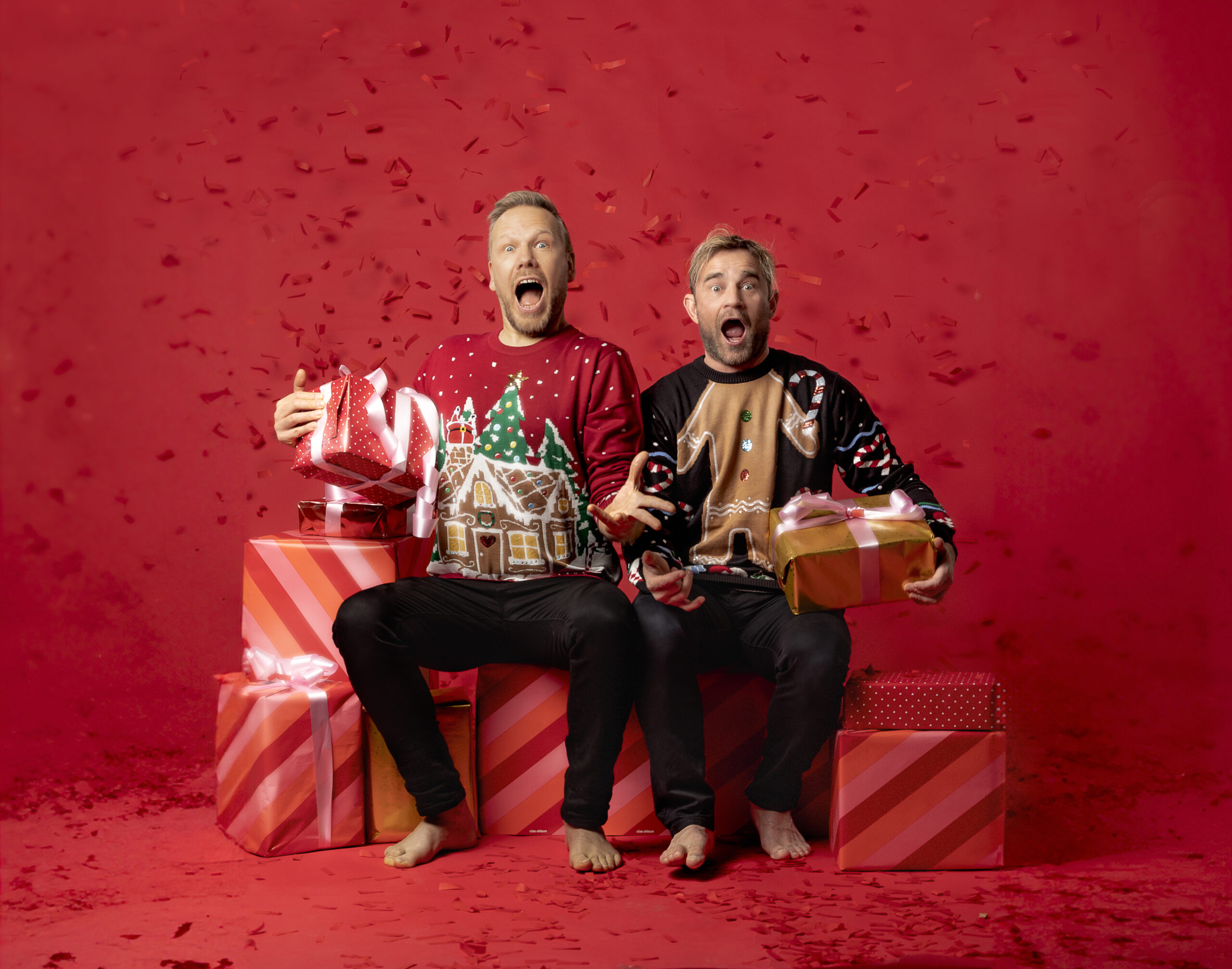 Kaksi joulupaitaista mieshahmoa istuvat lahjapakettien päällä ja ilmeilevät