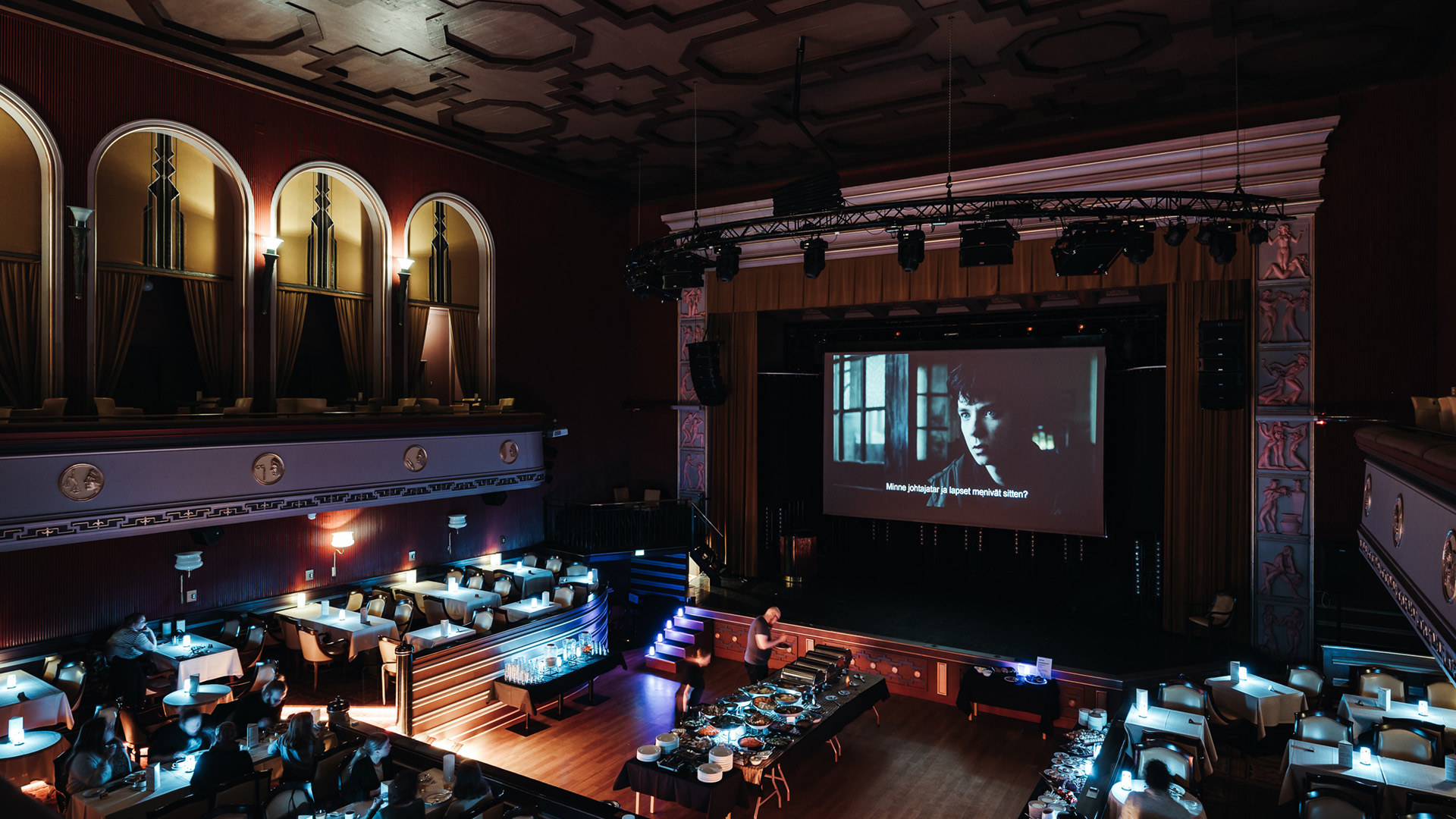 Tuulensuun Palatsin pääasali, jonka lavalle kankaalle heijastettu elokuva ja ihmisiä hakemassa salin keskeltä olevasta noutopöydästä syötävää.