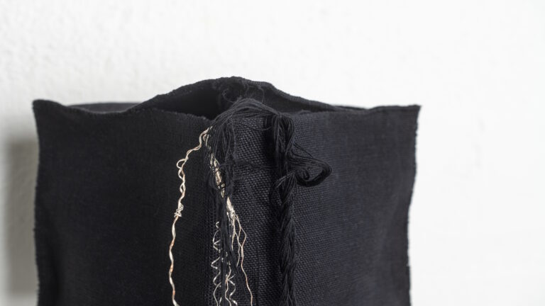 Valkoisella taustalla musta tekstiili, josta riippuu mustia ja vaaleita lankoja