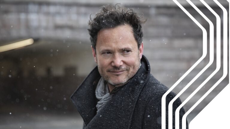Conductor standing and looking while it's snowing.