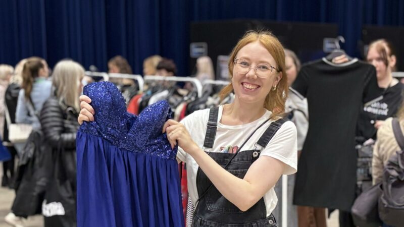 Nainen esittelemässä sinistä juhlamekkolöytöään swap-vaatteidenvaihtotapahtumassa.