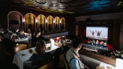 Audience watching the presentation from the balcony, with the art deco interior adding an elegant atmosphere.
