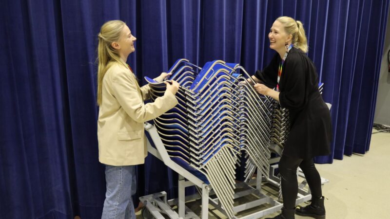 Tuotannon asiantuntijat nostavat tuoleja kärrystä nauraen