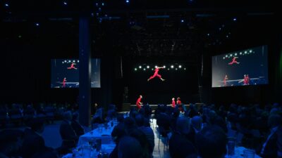 Sorin Sirkuksen esiintyjä ilmassa Infran Ammattipäivien iltatilaisuudessa Tampere-talossa, yleisön seuratessa esitystä pöydistä.